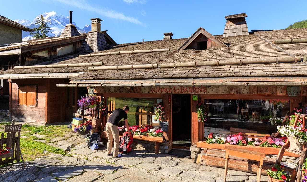 Auberge La Borne building with wood shingles, flowers, and snow-capped mountains in background.