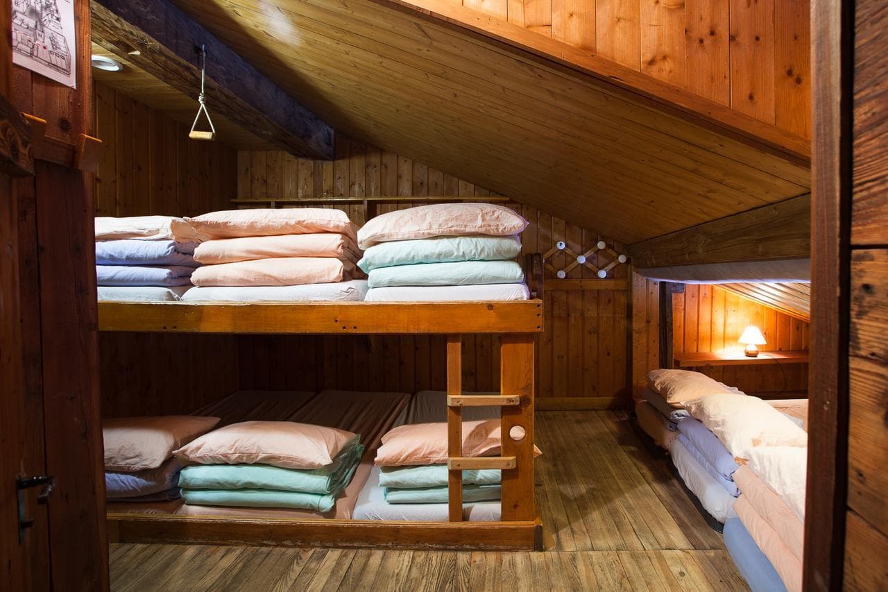 Wooden bunk beds and mattresses with stacked pink and blue linens in an attic room.
