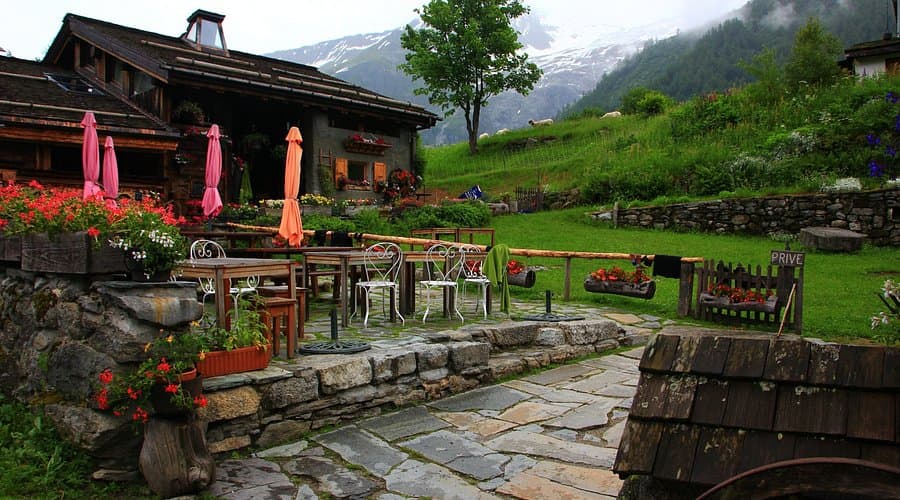 Outdoor dining terrace at Auberge la Boerne with stone patio, flowers, and snowy mountains.
