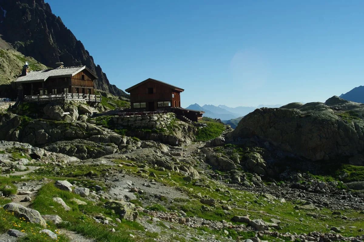 Wooden mountain refuge buildings on rocky terrain under a clear blue sky, Lac Blanc area