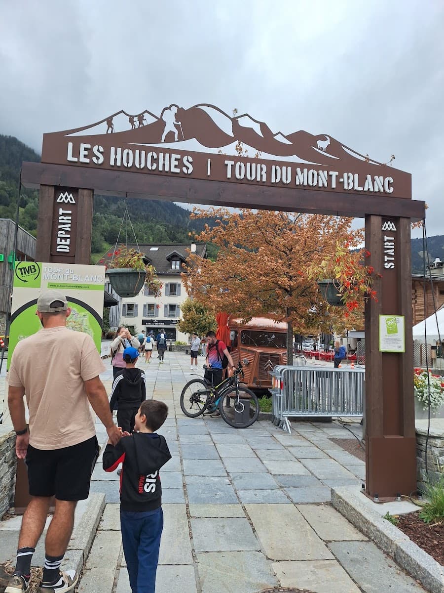 Tour du Mont-Blanc start arch and sign in Les Houches with people walking on paved square