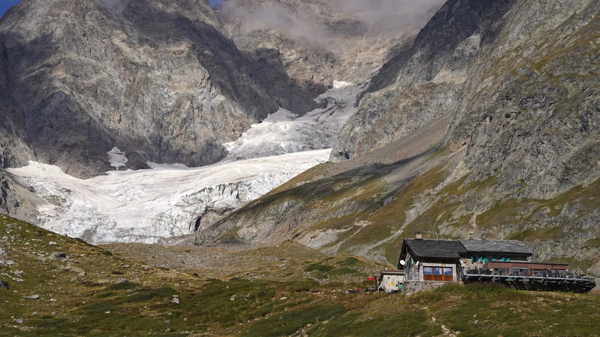 Rifugio Elisabetta mountain hut below a large glacier in rocky alpine terrain