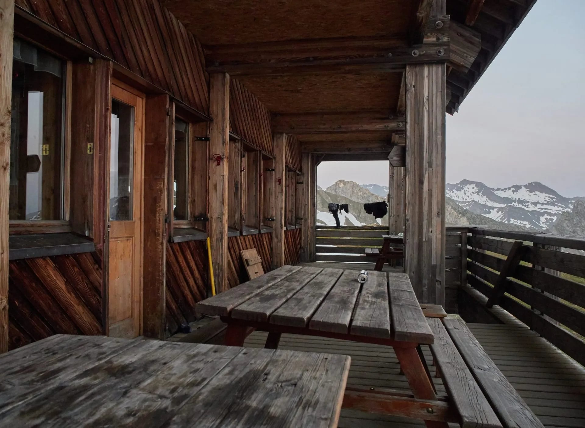 Wooden terrace of Refuge de la Croix du Bonhomme overlooking snow-capped mountains.