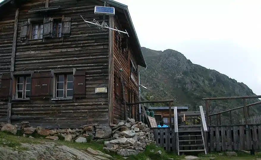Rustic wooden mountain refuge with solar panel next to a steep, rocky slope.