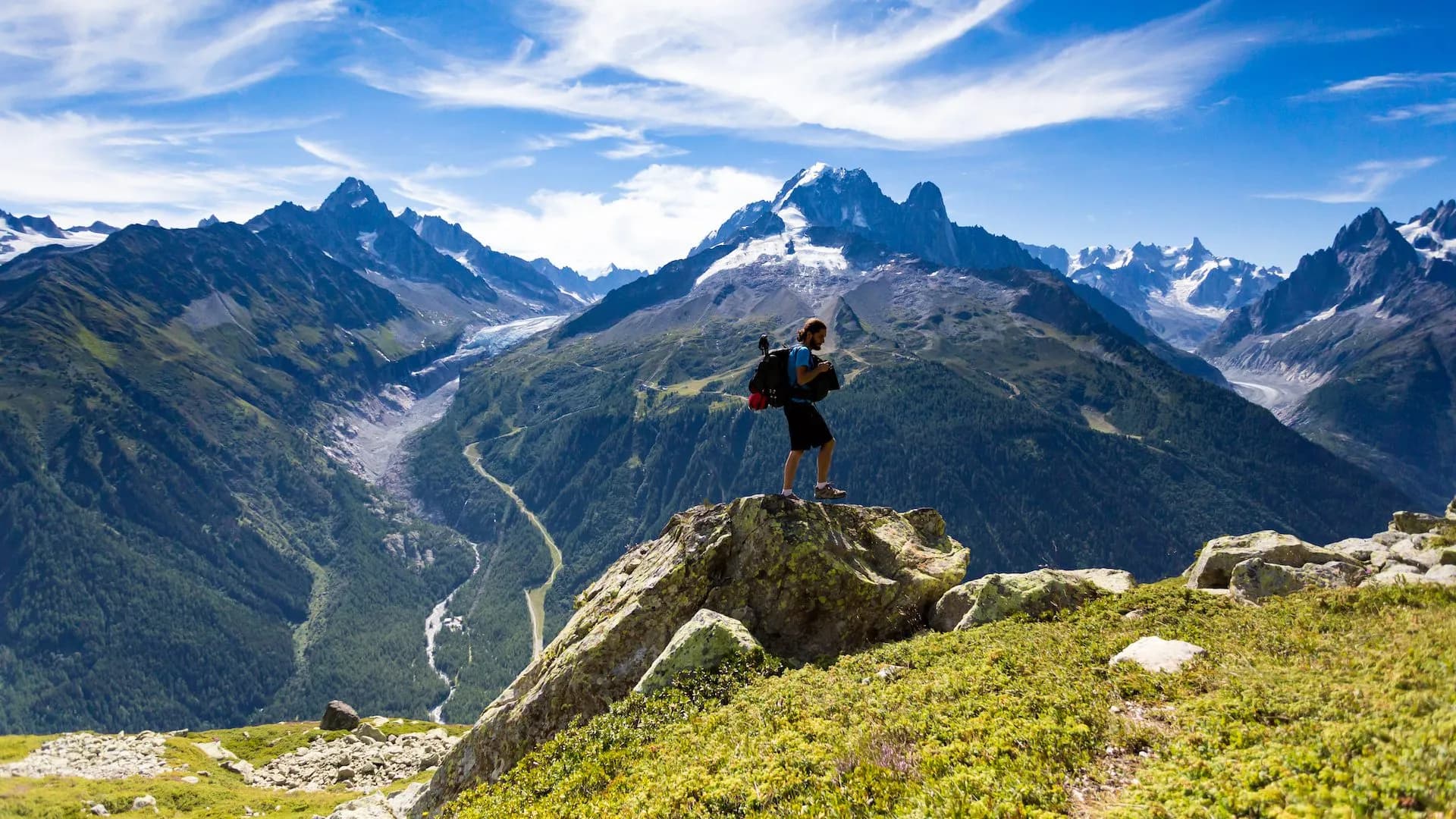 Hiker with backpack standing on rock overlooking vast mountains and glacier on Tour du Mont Blanc.