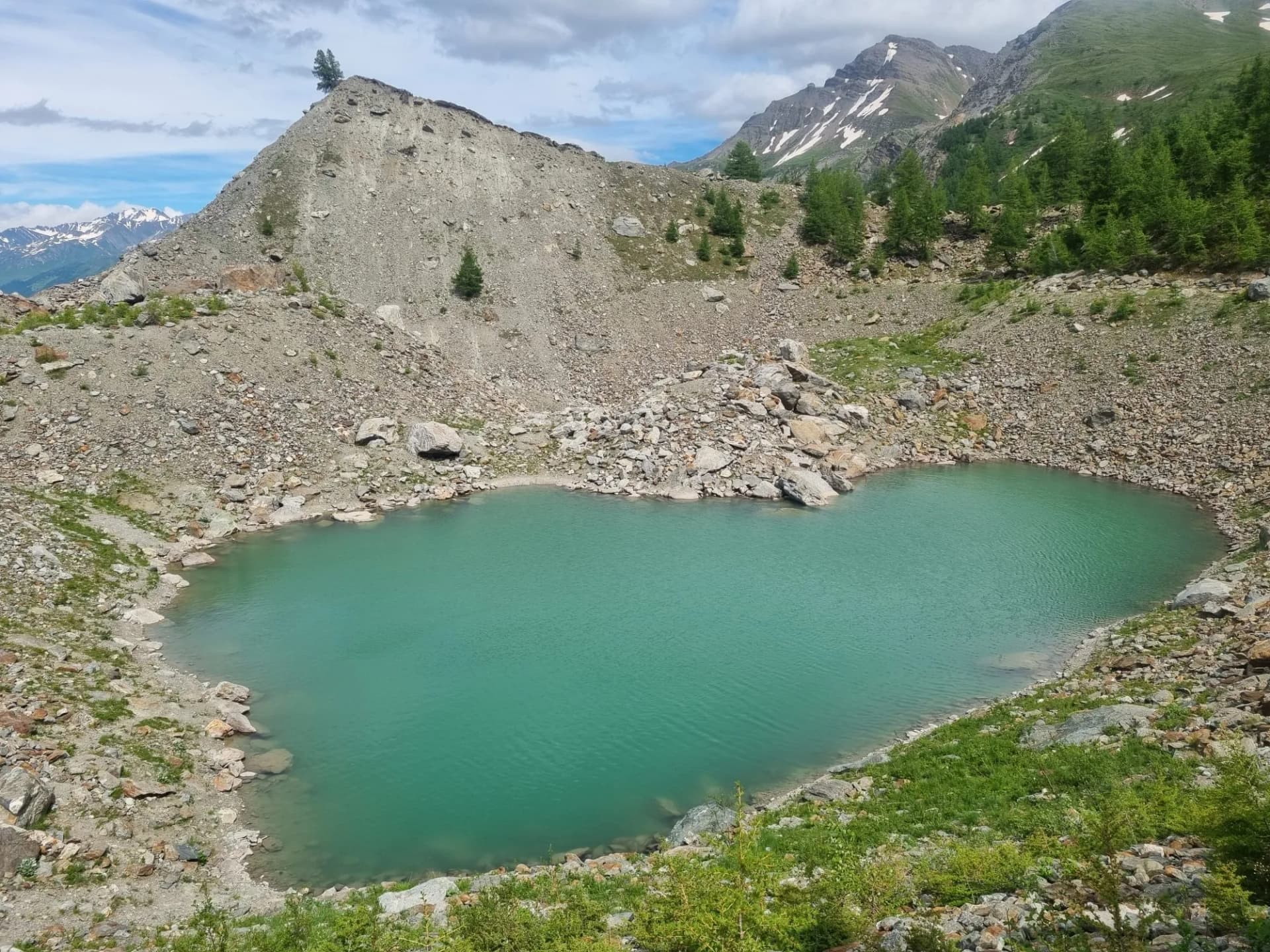 Turquoise alpine lake surrounded by rocky scree slopes and snow-capped mountains, Lago di Miage