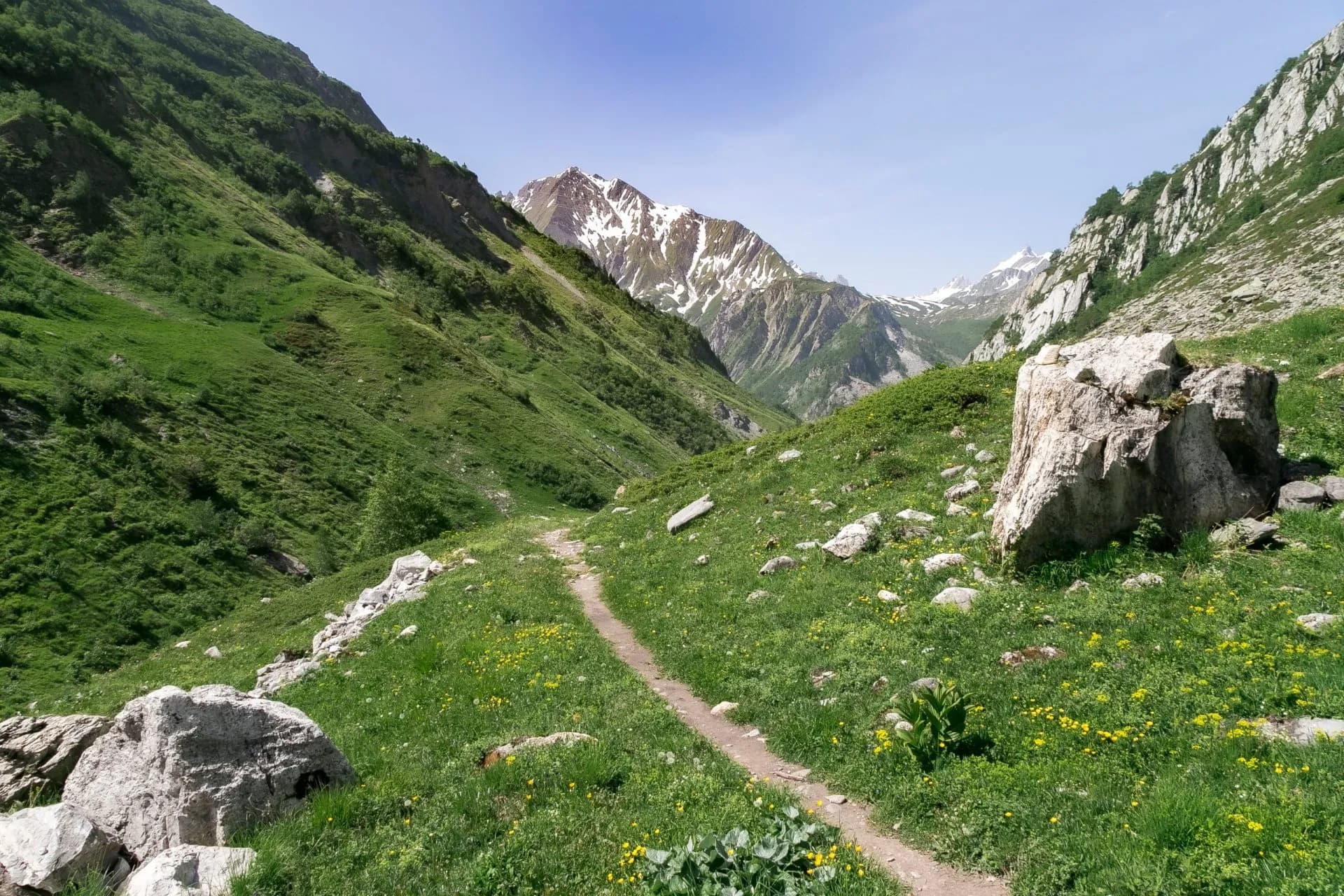 Hiking path through green alpine valley toward snow-capped mountains near Refuge des Mottets.