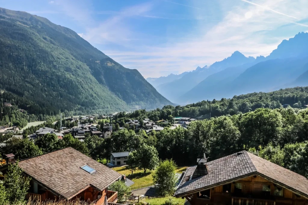 View of Les Houches village nestled in a green valley with forested mountains under a blue sky.
