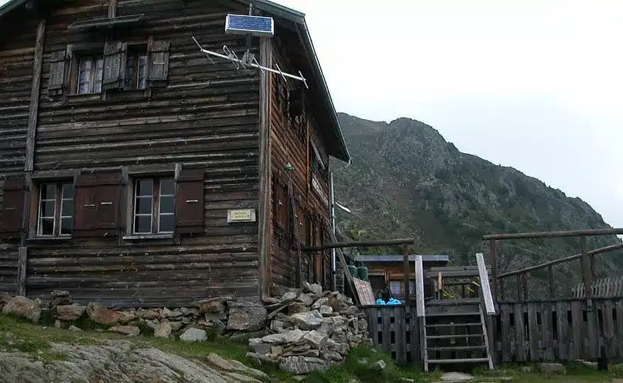 Rustic wooden mountain refuge with solar panel next to a steep, rocky slope.