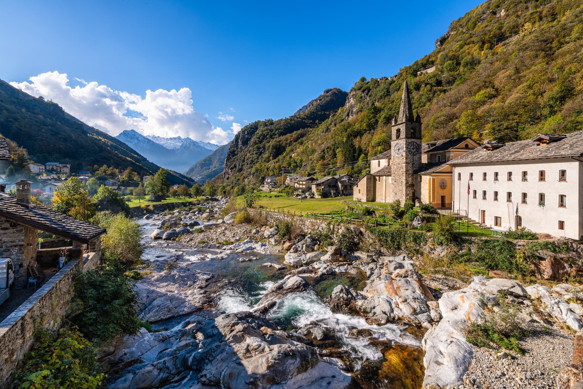 Alpine village with stone church beside a rocky river, mountains in background, Courmayeur.