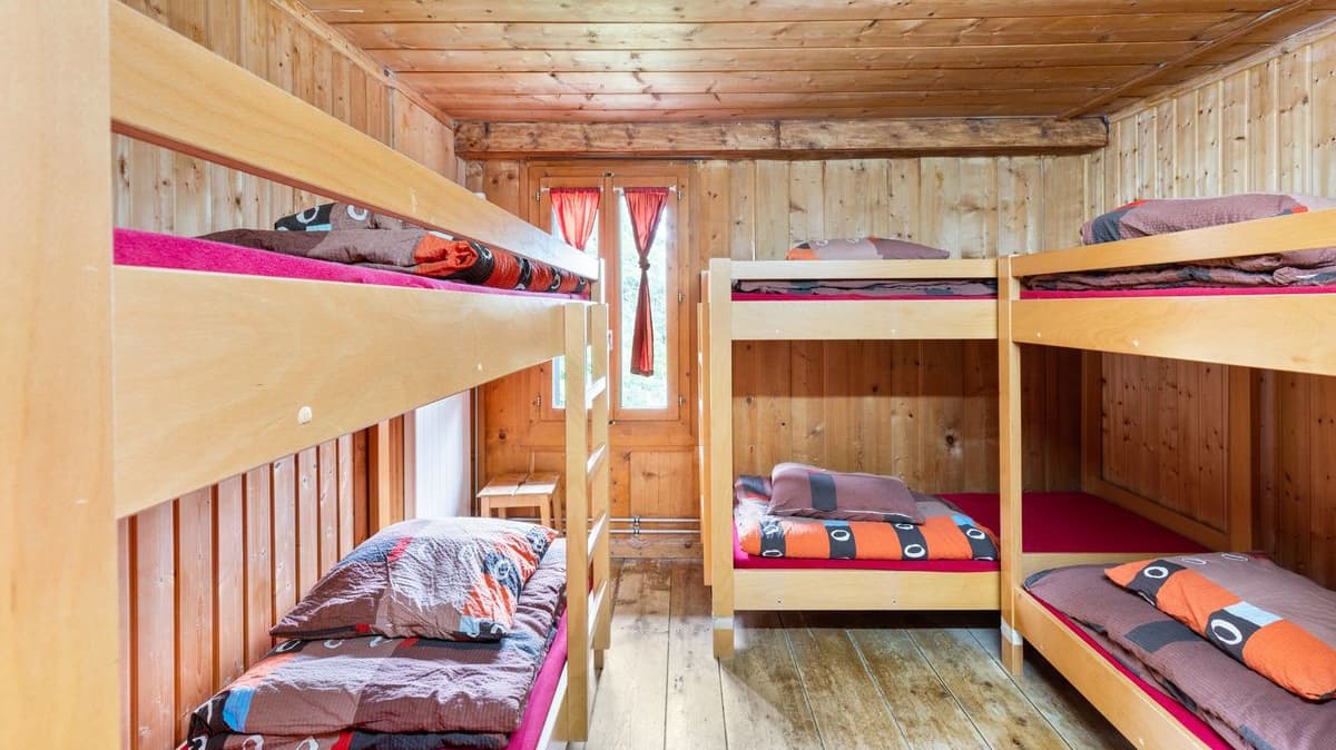 Wooden bunk beds with colorful bedding inside a rustic room with wood-paneled walls.