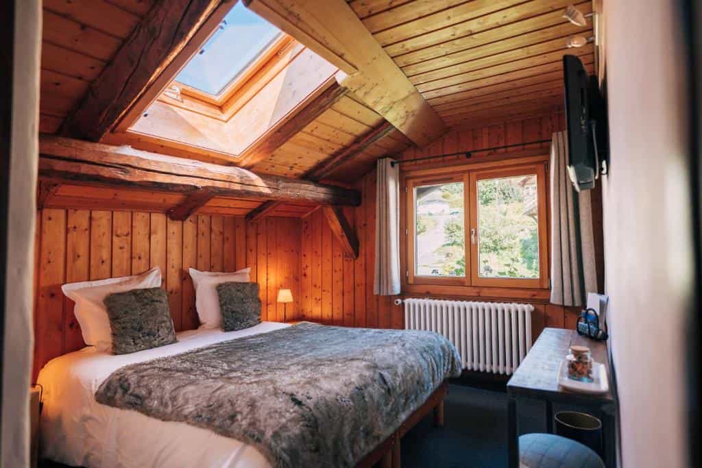 Cozy wooden attic bedroom with skylight, fur throw, and view of green hillside.