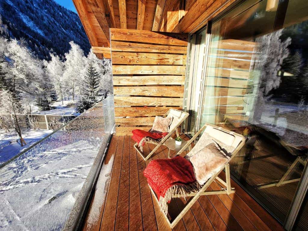 Wooden balcony with lounge chairs overlooking snow-covered alpine forest and mountains