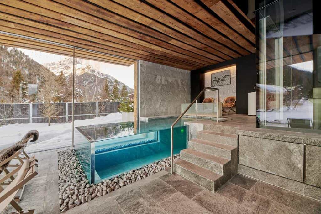 Indoor pool with glass sides overlooking snowy mountains and wooden ceiling