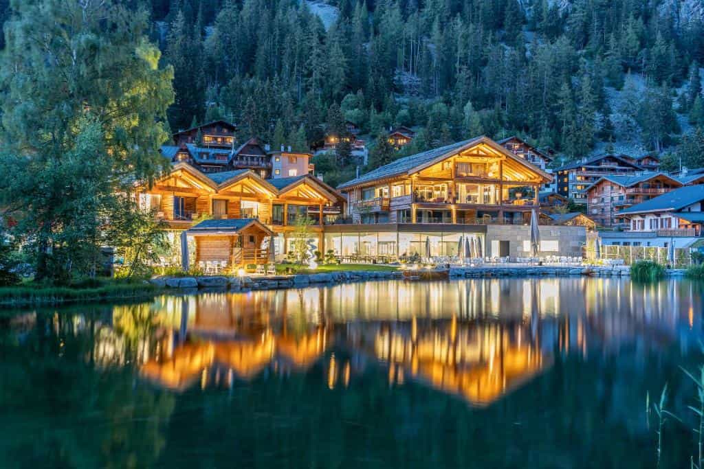 Illuminated wooden chalets reflected in a lake at dusk in an alpine village setting
