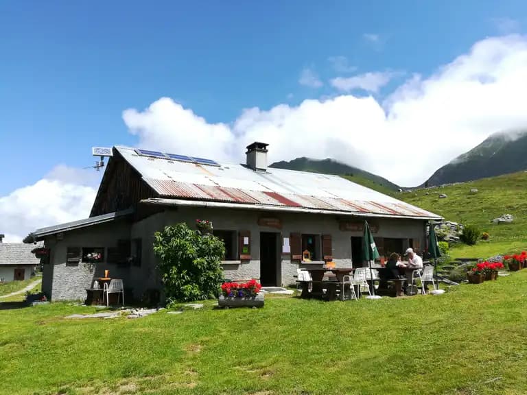 Stone mountain refuge with corrugated roof and outdoor dining area on grassy slope