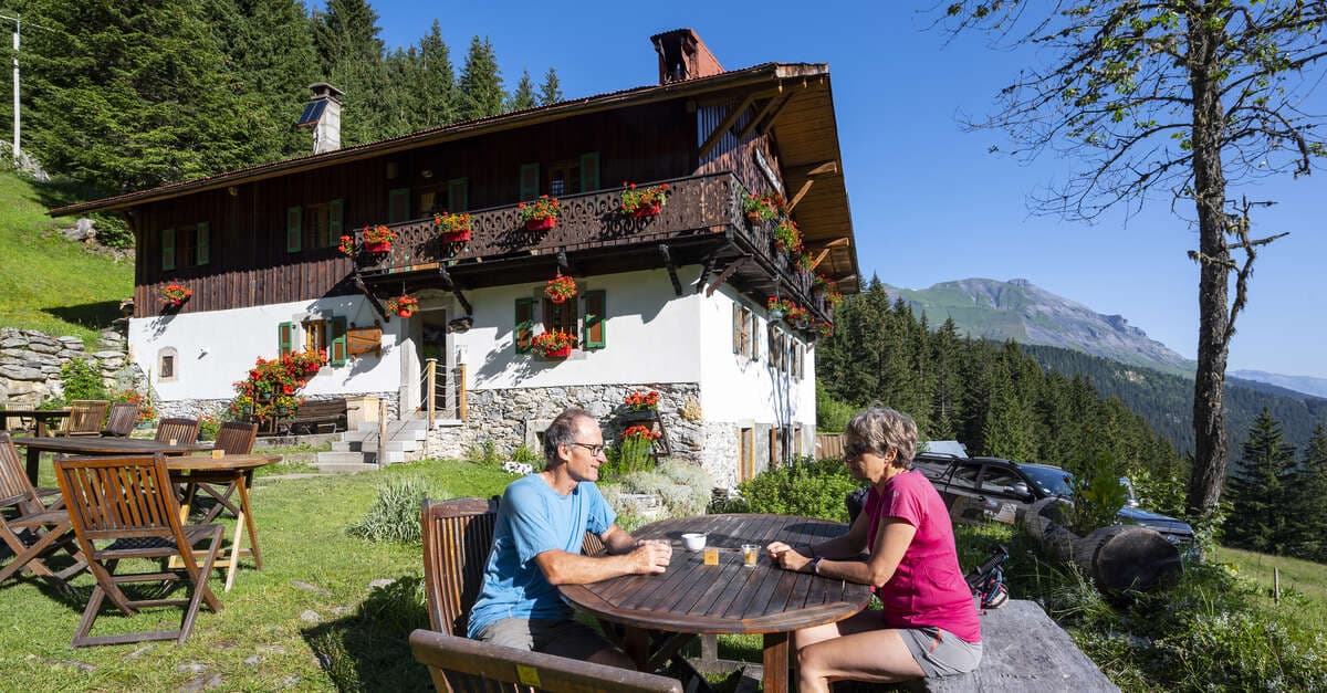 Couple resting at outdoor table near Refuge de Nant Borrant with alpine mountains.