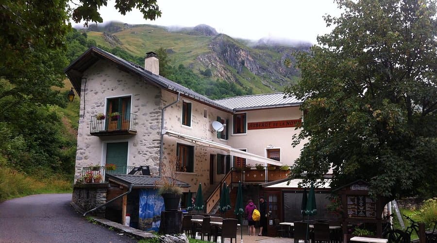 Auberge de la Nova building with outdoor seating against a backdrop of green, misty mountains.