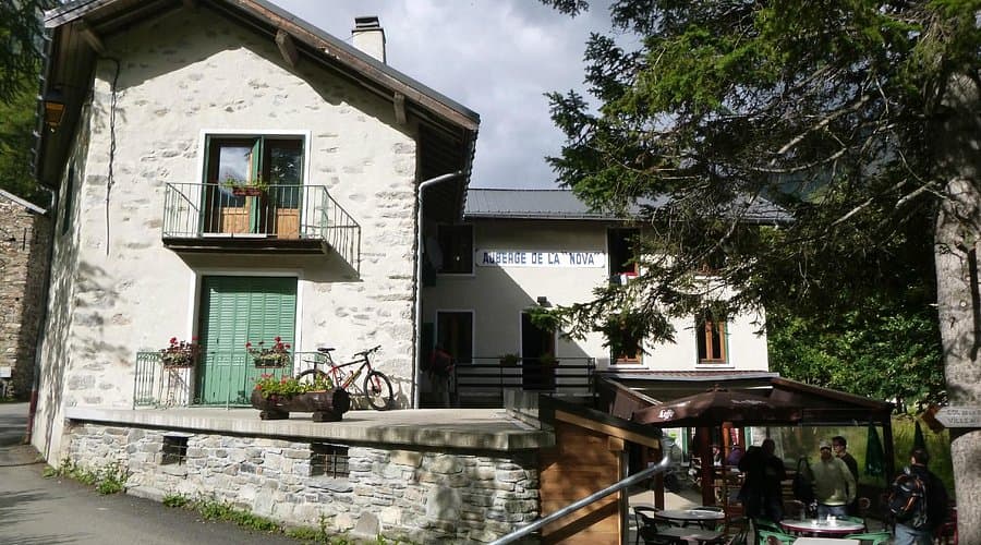 Auberge de la Nova building with stone base, bicycle parked outside, and outdoor seating area.