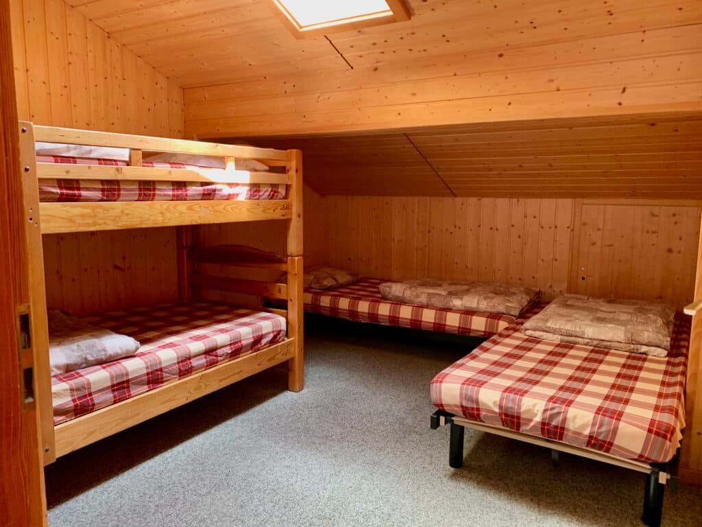 Bunk beds and single beds with red plaid bedding in a wood-paneled attic room at Relais d'Arpette.