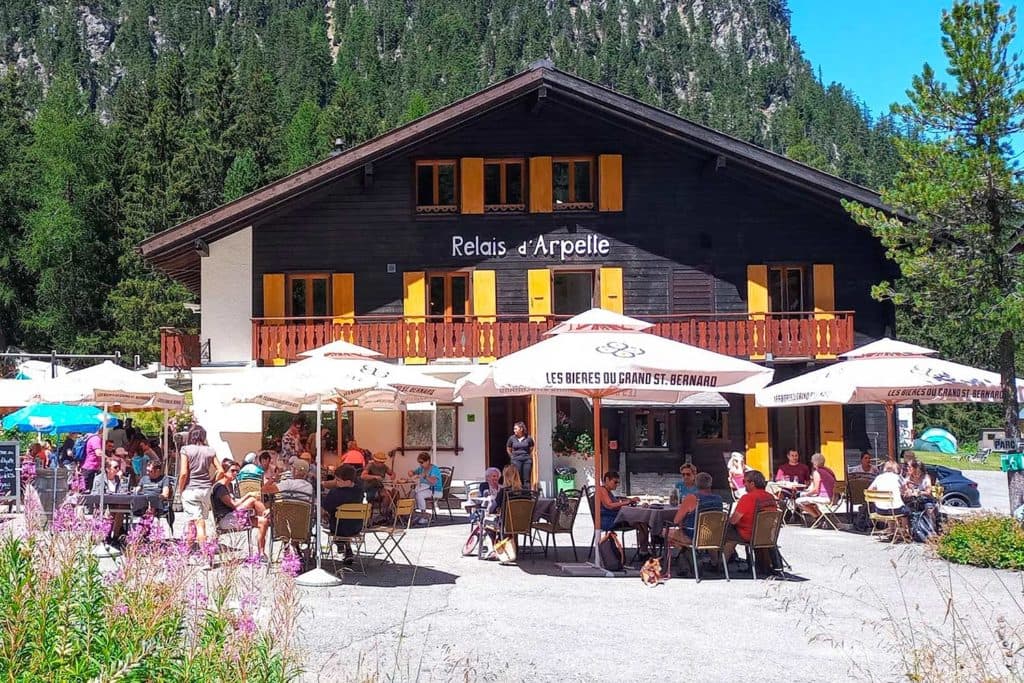 Relais d'Arpette restaurant with outdoor dining under umbrellas against a forested mountain backdrop.