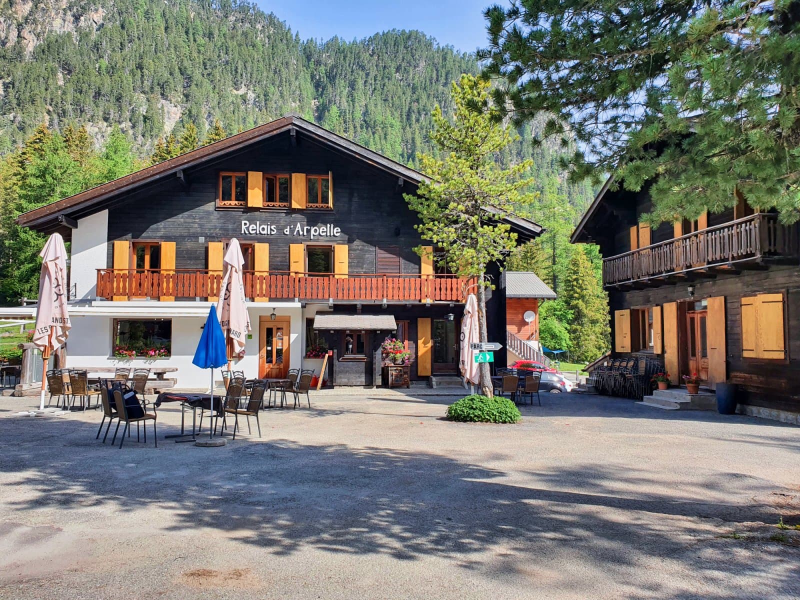 Relais d'Arpelle building with outdoor seating, set against a steep, forested mountain backdrop.