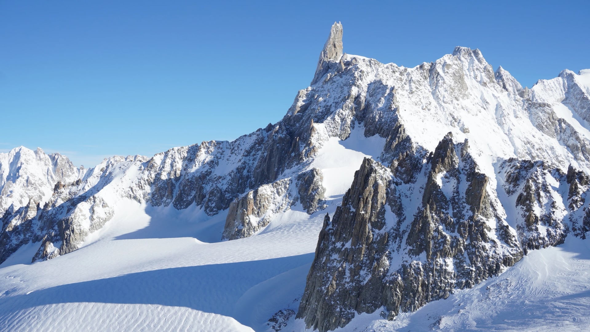 Panoramisk vinterlandskab af sneklædte alpine bjerge nær Mont Blanc i de italienske Alper. Pristine gletsjerlandskab, dramatiske toppe og uberørt natur under klar himmel.