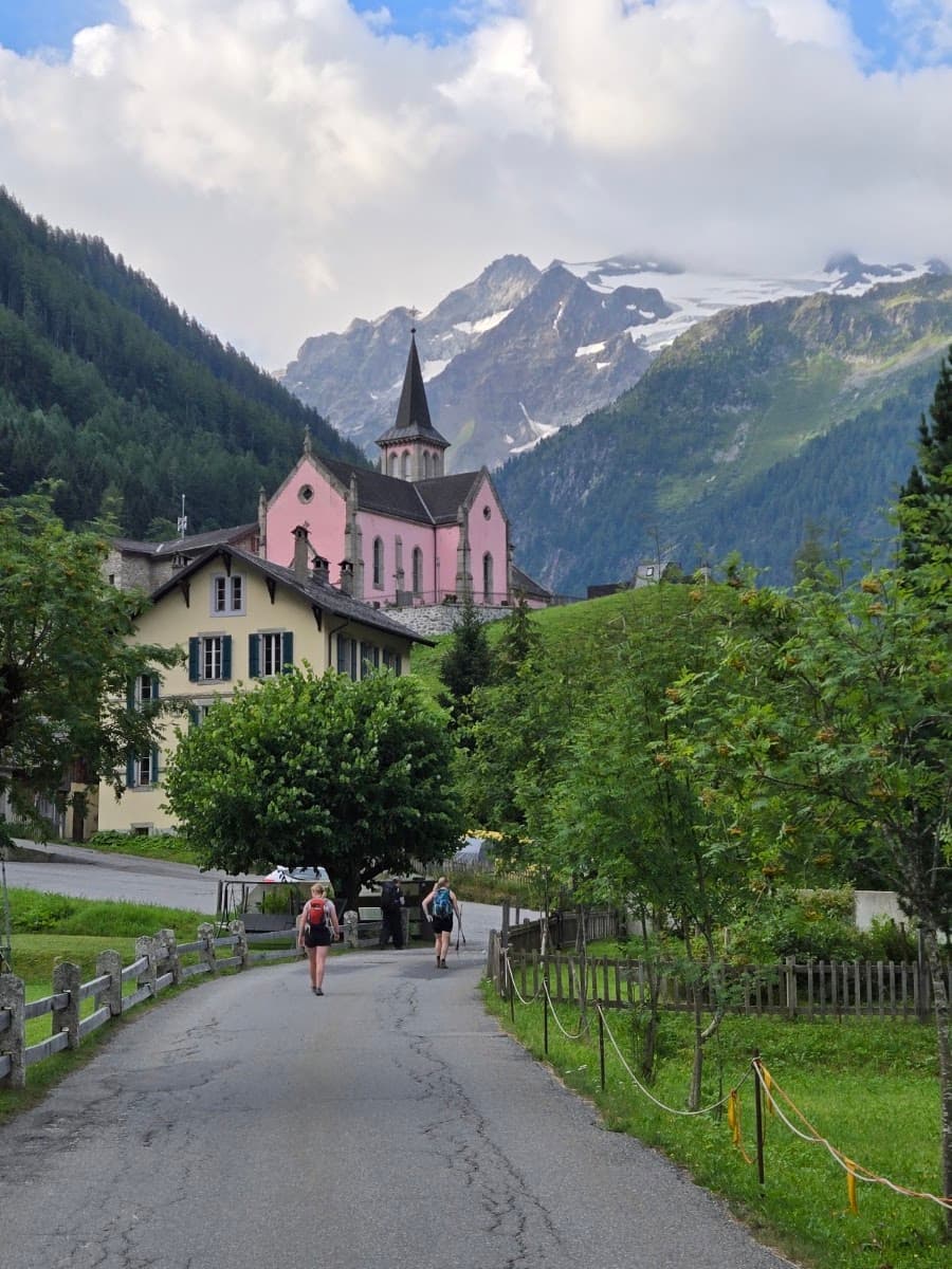 Hikers walking on road toward pink church and snow-capped mountains in alpine village