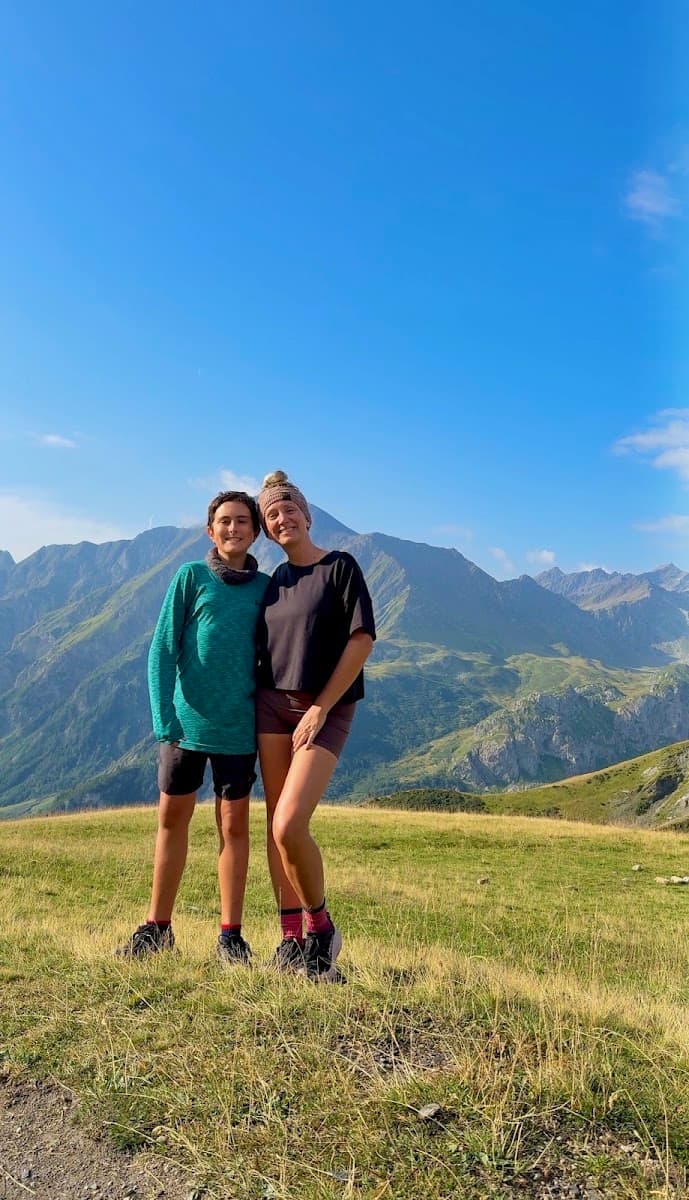 Two hikers standing on alpine mountain meadow with mountain peaks in background
