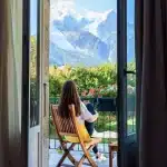 Beautiful young girl with long hair relaxing, drinking tea and enjoying amazing view at Mont Blanc mountain sitting at balcony in the morning.