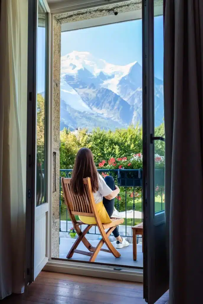 Vacker ung flicka med långt hår slappnar av, dricker te och njuter av den fantastiska utsikten över Mont Blanc-berget på en balkong på morgonen.